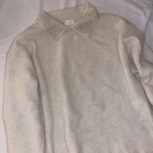 Vit tröja med pärlkrage HM - Säljer en stilren vit tröja från H&M med en elegant pärlbeströdd krage. Tröjan har långa ärmar och en mjuk, bekväm passform. Krämvit, endast använd en gång.