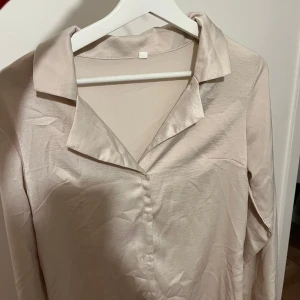 Beige blus med krage - Elegant beige blus med klassisk krage och knappar framtill. Perfekt för en stilren look. Minns inte exakt vart den kommer ifårn men tror Hm, är i storlek S