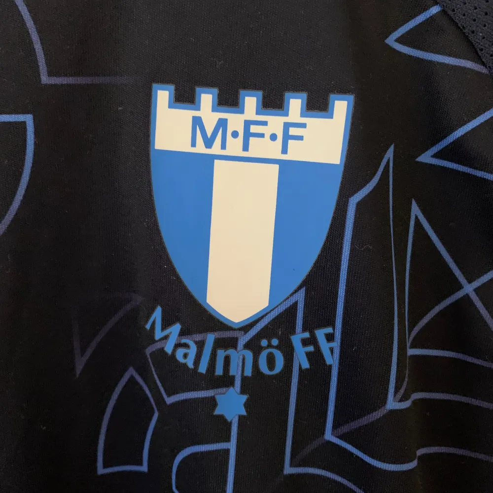 Säljer en snygg Malmö FF fotbollströja från Puma. Den är mörkblå med ett coolt geometriskt mönster i ljusblått. Tröjan har korta ärmar och klubbens emblem på bröstet. Perfekt för alla MFF-fans!. T-shirts.