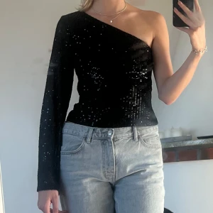 Svart paljettopp med en axel - Säljer en superfin svart paljettopp som är oneshoulder. Den har en lång ärm och är perfekt för festliga tillfällen. Perfekt för en utekväll eller nyårsfesten! ✨