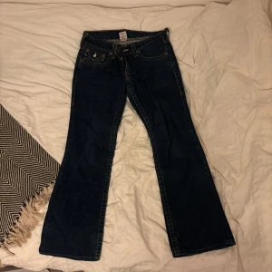 Mörkblåa True Religion - Ett par mörkblåa jeans från True Religion. Det är storlek 30 i midja och 33 i höften. Byxorna är smått nedgångna längst ner, men inte så illa, annars är dem överlag i riktigt bra skick! Jag är 166 och byxorna är ca 3 cm för långa för mig!
