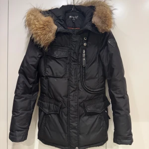 Hollies Jacka i storlek 34 - Helt ny Hollies Jacka. Köpt för ca 5500 (ny pris). Används några fåtal gånger förra vintern. Äkta päls krage på luvan. Fyllningen är av 80% dunn och 20% fjäder. Nyskick men det saknas en knapp. Annars inga repor eller skador. För frågor eller fler bilder skicka iväg ett meddelande :)