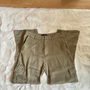 Beige cargobyxor från Pull&Bear - Säljer ett par snygga gröna cargobyxor från Pull&Bear. De har en loose passform och är perfekta för en avslappnad stil. Byxorna har flera praktiska fickor och en dragkedja framtill. Perfekta för höst och vår!