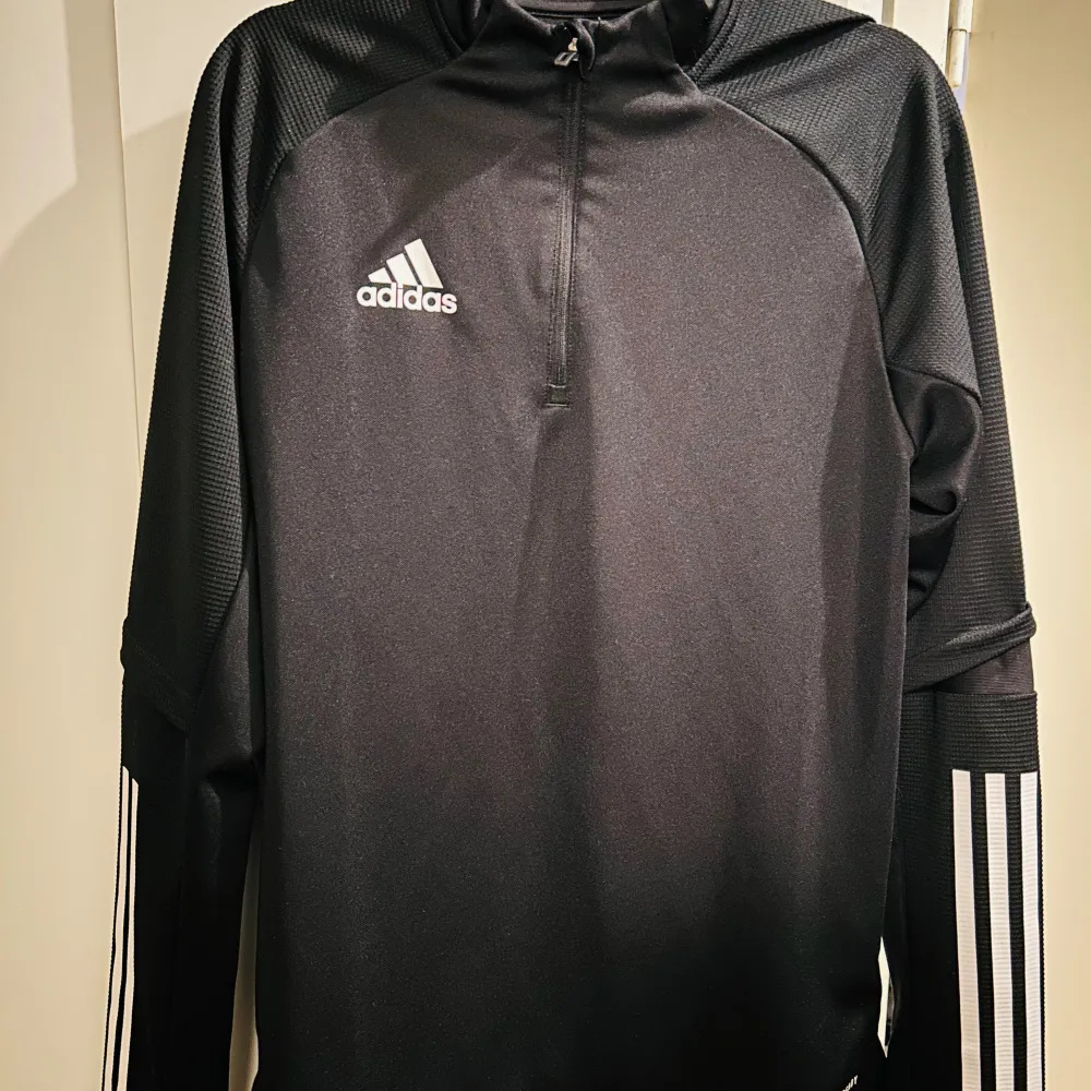 Säljer en snygg och sportig svart långärmad tröja från Adidas. Den har en halv dragkedja framtill och de klassiska tre ränderna på ärmarna. Perfekt för träning eller en avslappnad dag. Materialet är AEROREADY, vilket gör den bekväm och andas bra. . Tröjor & Koftor.