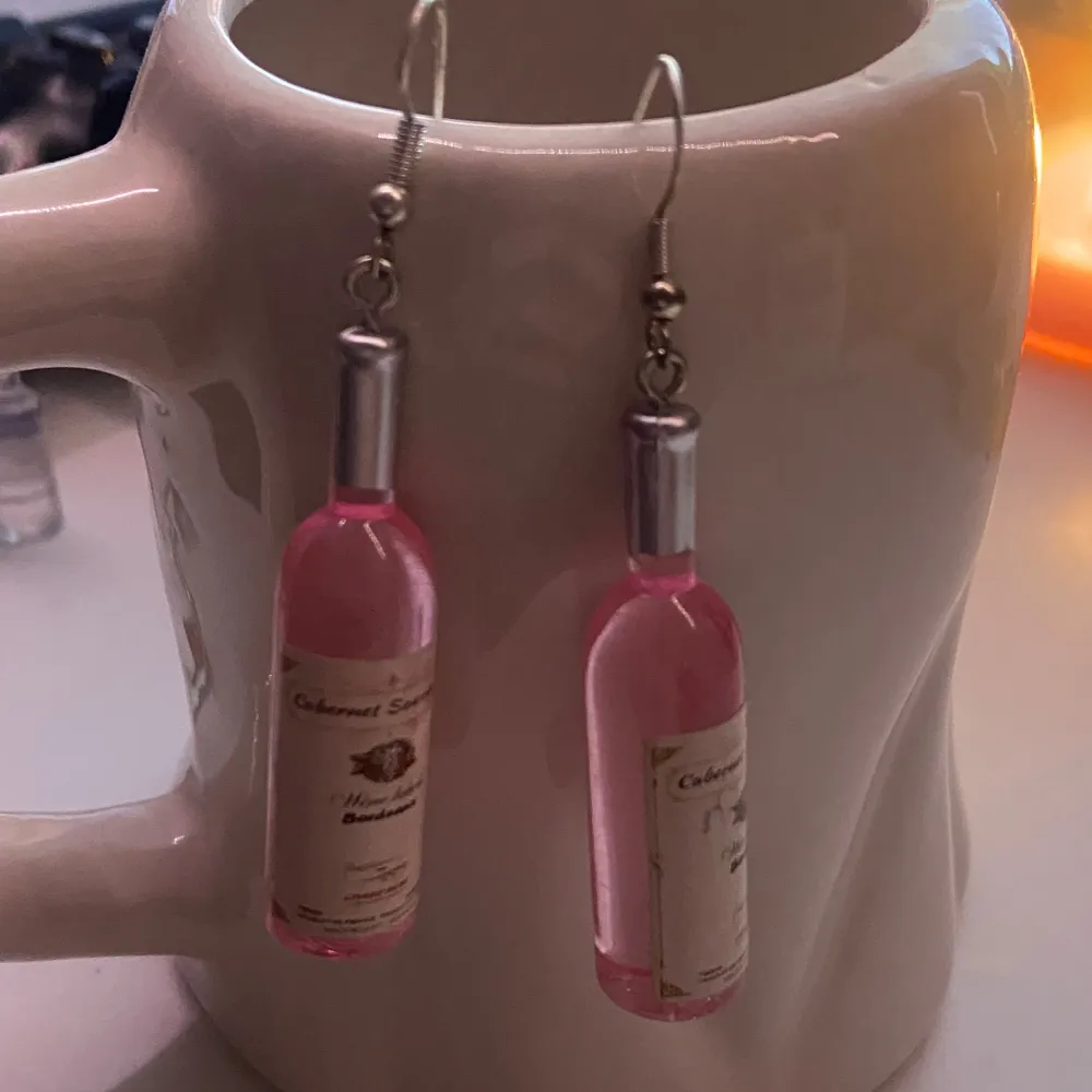 Supercoola örhängen formade som små rosa vinflaskor med etikett. Perfekta för en festlig look eller som en rolig accessoar till vardags. De har en krok i silverfärg för enkel användning. Ett måste för vinälskare som vill sticka ut!. Accessoarer.