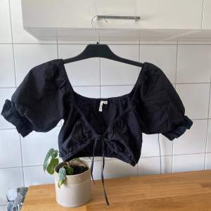 Säljer en superfin svart croppad blus med puffiga kortärmar. Den har en söt knytning framtill och är perfekt för sommardagar eller festliga tillfällen. Passar bra till både jeans och kjol!