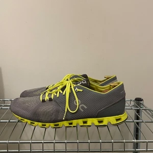 On Running träningsskor - Grå/neon färgade träningsskor ifrån ON Running Cloud. Använda med lite slitage i hälen annars i mycket fint skick.