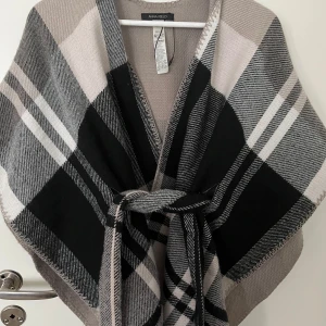 Jätte fin poncho  - Fin poncho som används 1 gång. Ligger bara i garderoben.  Storlek: one size  Färg: svart, vit och beige.   PRIS KAN DISKUTERAS! 