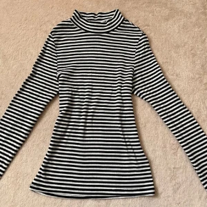 Randig polotröja i svart och vit - Snygg randig polotröja i svart och vit. Tröjan har en tight men stretchig passform. Använd några gånger, fint skick strl XS.