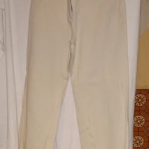 Beige byxor från Sandwich - Snygga beige byxor från Sandwich med en klassisk design. Byxorna har en rak passform och är perfekta för en stilren look. De är tillverkade i ett bekvämt material och har praktiska fickor baktill.