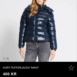Kort pufferjacka 'Nikki' - Snygg och glansig mörkblå pufferjacka från 157. Jackan är kort och har en praktisk dragkedja framtill. Perfekt för kyliga dagar med sin vadderade design och huva. 