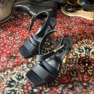 Svarta sandaler med klack från Tommy Hilfiger - Snygga svarta sandaler från Tommy Hilfiger med breda remmar och en justerbar spänne i guld. Sandalerna har en träliknande klack som ger en elegant touch. Perfekta för sommarens alla tillfällen. Pris från butik 1800sek