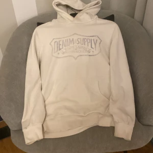 Vit/beige hoodie från Denim & Supply Ralph Lauren - Säljer en vit/beige hoodie från Denim & Supply Ralph Lauren. Tröjan har en stor logga på framsidan och är tillverkad i en mjuk bomullsblandning. Storlek:S.