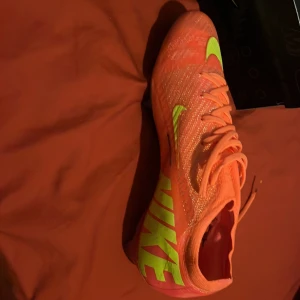 Nya Nike Mercurel. Endast använda en träning, men är för smal för min fot. Helt ny modell redan slutsåld hos många. Ta chansen och få säsongens snyggaste skor för en billigare peng!  - Snygga och färgstarka Nike Mercurial fotbollsskor i orange med neongula detaljer. Skorna har snörning och en modern design som passar perfekt för fotbollsplanen. Inkluderar en praktisk Mercurial-väska.