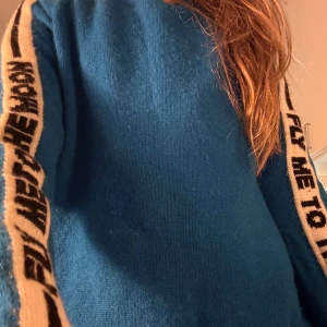 From future tröja (klicka inte på köp nu) -  Säljer för jag har inte använt den på långe Snygg blå tröja med texten 'FLY ME TO THE MOON' längs ärmarna. Perfekt för en avslappnad stil med en unik touch. Tröjan har långa ärmar och en normal passform.