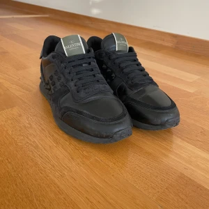 Svarta sneakers från Valentino Garavani - Snygga svarta sneakers från Valentino Garavani med coola nitar på sidorna. Skorna har en kombination av skinn och mocka, vilket ger en lyxig känsla. Perfekta för dig som vill ha en stilren look med en edgy touch. original innersulor tillkommer ej då endast extra spikar ingår