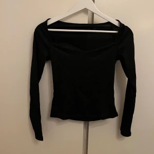 Svart ribbad topp - OANVÄND - Snygg svart ribbad topp med långa ärmar och en elegant v-ringad design. Perfekt för en stilren look. Helt oanvänd!