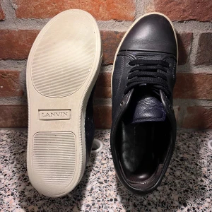 Svarta sneakers från Lanvin - Snygga svarta sneakers från Lanvin i skinn med vita sulor. Skorna har klassisk snörning och en stilren design som passar perfekt till vardags. Perfekta för dig som vill ha en kombination av stil och komfort. Storkek UK 7 men passar 42. No box. 