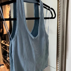 Ljusblå ribbad linnetopp - Snygg ljusblå ribbad linnetopp med smala axelband och rund halsringning. Perfekt för varma sommardagar eller som ett lager under en jacka. Enkel och stilren design som passar till många olika outfits.