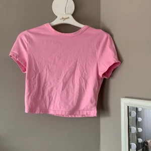 Rosa croppad t-shirt från Shein - Säljer en söt rosa croppad t-shirt från Shein. Perfekt för sommardagar med sin korta längd och mjuka bomullsmaterial. Enkel och stilren design som passar till det mesta.