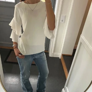 Vit blus med volangärmar - Säljer en stilren vit blus med volangdetaljer på ärmarna. Blusen har en normal passform och är perfekt för både vardag och festliga tillfällen. Den är tillverkad i ett mjukt och bekvämt material.