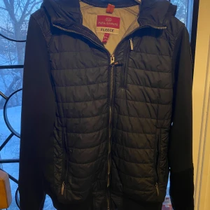 Svart cardigan från Parajumpers - Säljer en svart fleecejacka från Parajumpers med quiltad design och dragkedja. Jackan har en huva och långa ärmar, perfekt för kyliga dagar. Den är både stilren och funktionell. Pris kan diskuteras och sänkas vid snabbt köp!!!