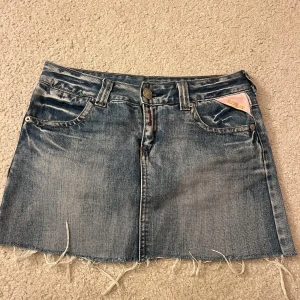 Jeanskjol från Replay - Snygg jeanskjol från Replay i en klassisk blå färg. Kjolen har en kort längd med fransig nederkant och orange dragkedjor på bakfickorna. Den har också en rosa detalj med Replay-loggan vid fickan fram. Midjemått: 38cm rakt över. Längd: 32cm. Använd gärna köp nu 💕💕