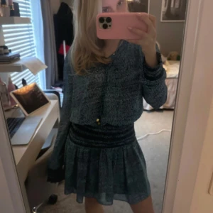 Blå klänning med volangdetaljer - Charmig blå klänning med volangdetaljer och långa ärmar. Perfekt för en stilfull look med sin korta längd och mjuka material. 