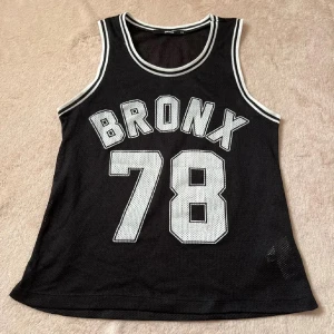 Svart tränings linne - Svart träningslinne med vita kanter och texten 'Bronx 78'. Perfekt för en sportig look eller avslappnad stil. strl XS