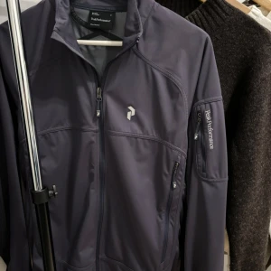 Peak Performance vindjacka/kofta - Snygg zip-up vindjacka/kofta från Peak Performance med dragkedja och flera praktiska och stora fickor . Perfekt för utomhusaktiviteter med stilren design och logga på bröstet, ärmen och kragen. Nypris: 599kr