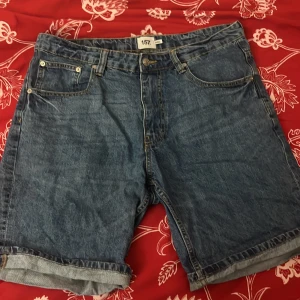 Blå jeansshorts från 157 - Säljer ett par klassiska blå jeansshorts från 157. De har en normal passform med fem fickor och knappgylf. Perfekta för en avslappnad stil.