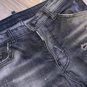 Svarta jeans från Dsquared2 - Snygga svarta jeans från Dsquared2 med slitna detaljer och en cool tvätt. De har en klassisk femficksdesign och en knappgylf. Perfekta för en trendig look. Den har en defekt och det är lappen där bak. Priset är inte hugget i sten kan gå ner vid snabb affär. Mvh