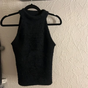 Svart ärmlös topp från Nelly - Snygg svart ärmlös topp från Nelly i fluffigt material. Perfekt för en stilren look med hög krage. Passar utmärkt till både jeans och kjol.