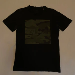 Svart t-shirt från Adidas med kamouflagemönster - Säljer en svart t-shirt med camoprint från adidas. Storlek s, är i bra skick. Säljer pga för liten.