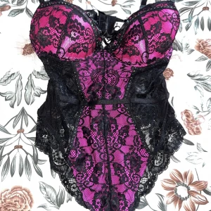Svart och rosa spetskorsett - Elegant korsett i svart och rosa med spetsdetaljer. Den har justerbara axelband och en hakknäppning bak. Perfekt för en speciell kväll. HELT OANVÄND!!