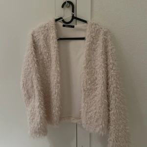 Beige teddykofta från Gina tricot  - Mysig beige teddykofta med fluffig textur. Perfekt för att hålla sig varm och stilren under kyliga dagar. Koftan/jackan har en öppen design utan knappar eller dragkedja.