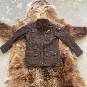 Brun quiltad jacka från Barbour - Säljer en snygg brun quiltad jacka från Barbour International. Jackan har en klassisk design med krage och flera praktiska fickor med knappar. Perfekt för höst och vår med sin stilrena look och funktionella detaljer. Pris kan diskuteras 