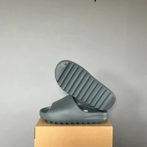 Yezzy slide - Köpte nya yezzy slide till min brorsa men de passade inte honom. Svart gråa yezzy slide från adidas och yezzy. Storlek 42,5. Nytt skick. Kommer med boxen och tagsen.