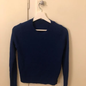 Blå stickad tröja - Säljer en snygg blå stickad tröja med rund halsringning. Tröjan har långa ärmar och en klassisk passform som passar perfekt för kyligare dagar. Perfekt för att hålla sig varm och stilren.