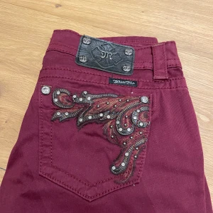 Vinröda miss Me jeans med broderade detaljer - Snygga vinröda jeans från Miss Me med unika broderade detaljer och nitar på bakfickorna!🤗Helt oanvända med lapp!💕 Jeansen har en normal passform och är perfekta för att ge din outfit en extra touch. Säljer då de var lite för stora! De är skinny jeans men det är lätt att sy om de till din föredragna stil!! Kontakta om ni vill ha mer info!💖💖