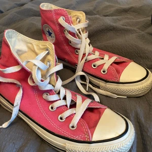 Rosa Converse All Star sneakers - Säljer ett par klassiska rosa Converse All Star sneakers med hög modell och vita snören. Skorna har den ikoniska loggan på sidan och en vit gummisula med svart rand.