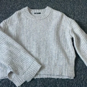 Grå stickad tröja från Gina Tricot - Mysig grå stickad tröja från Gina Tricot. Perfekt för kyliga dagar med sin ribbade design och långa ärmar med slits ner till och slits på sidorna. Enkel och stilren, passar till det mesta i garderoben.