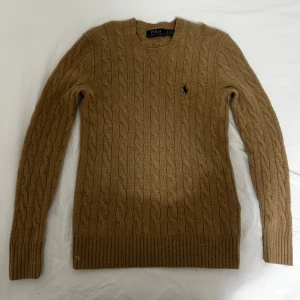 Beige kabelstickad tröja från Polo Ralph Lauren, nypris 2600kr - Säljer en stilren beige kabelstickad tröja från Polo Ralph Lauren. Tröjan har en klassisk rund hals och det ikoniska logotypbroderiet på bröstet. Perfekt för en elegant och avslappnad look. Köpt på nk för 2 år sen. Den e storlek xs men skulle kunna passa storlek s om du är smalare. Nästan inga defekter. Använt den 2 gånger. 90% bomull, 10%kashmir