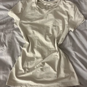 Vit t-shirt från H&M - Säljer en klassisk beige t-shirt från H&M i storlek S. T-shirten är kortärmad och tillverkad i ett mjukt bomullsmaterial. Perfekt basplagg för alla tillfällen.