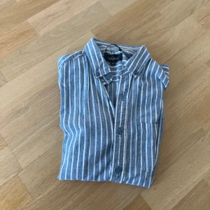 Blå och vit randig skjorta från L.L.Bean - Snygg blå och vit randig skjorta. Skjortan har en klassisk krage och knappar framtill. Perfekt för en stilren look.