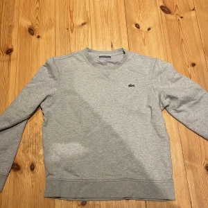 Grå lacoste sweatshirt   - Säljer en stilren grå sweatshirt från Lacoste med det klassiska krokodilmärket på bröstet. Tröjan har långa ärmar och en rund halsringning. Perfekt för en avslappnad look. Strl s