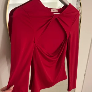 Röd långärmad topp från Nelly - Snygg röd topp från Nelly med lång ärm och unik draperad design framtill. Perfekt för en kväll ute eller en speciell tillställning. 