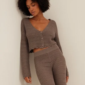 Brun stickad kofta från NA-KD - Säljer en snygg brun virkad kofta från NA-KD. Koftan har en v-ringad design med knappar framtill och är croppad för en modern look. 