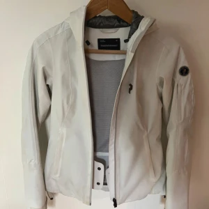 Vit jacka från Peak Performance - Snygg vit jacka från Peak Performance, precis köpt från Vinted men satt inte som jag ville. Den är storlek 38 men skulle snarare säga 34/36. Den är i fint skick men lite lite missfärgad längst, det går säkert bort om man vill ta tag i det! Figurnära passform med många fickor. 