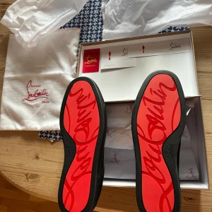 Nya Svarta från Christian Louboutin - Snygga svarta sneakers från Christian Louboutin med den ikoniska röda sulan. Perfekta för att ge din outfit en lyxig touch.